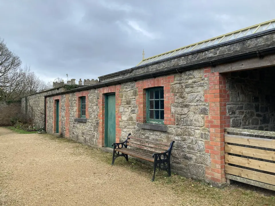 Side view of the stables: mainly built with stone, door and window frames are highlighted by red brick. Entry doors and windows' rails are painted green.
