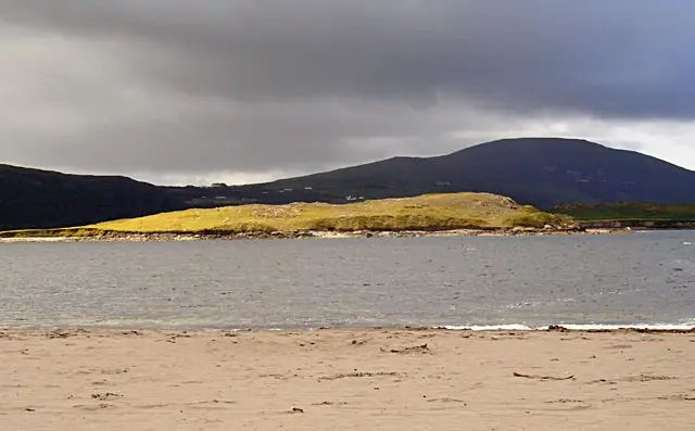 Beginish Island, viewed from White Strand Beach Beginish Island highlighted by the sunlight, with Valentia Island in the shadow behind. Seen from White Strand beach, V4379.