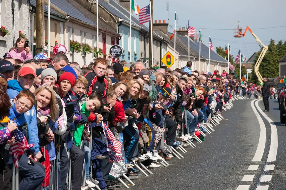 A crowd of onlookers watches as United States President Barack Obama and First Lady Michelle Obama walk east along Main Street in Moneygall, County Offaly, Ireland, 23 May 2011.